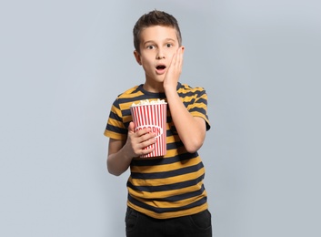 Emotional boy with popcorn during cinema show on grey background