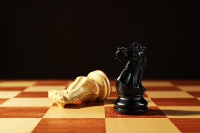 Photo of Wooden black knight and fallen one on chessboard against dark background. Competition concept