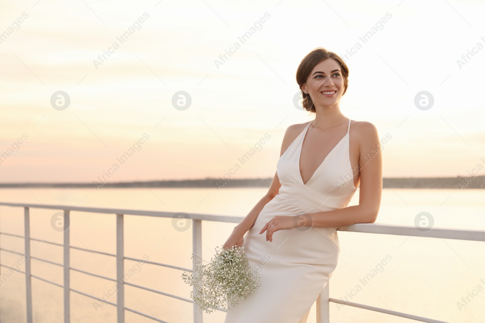 Photo of Gorgeous bride in beautiful wedding dress with bouquet near river on sunset. Space for text