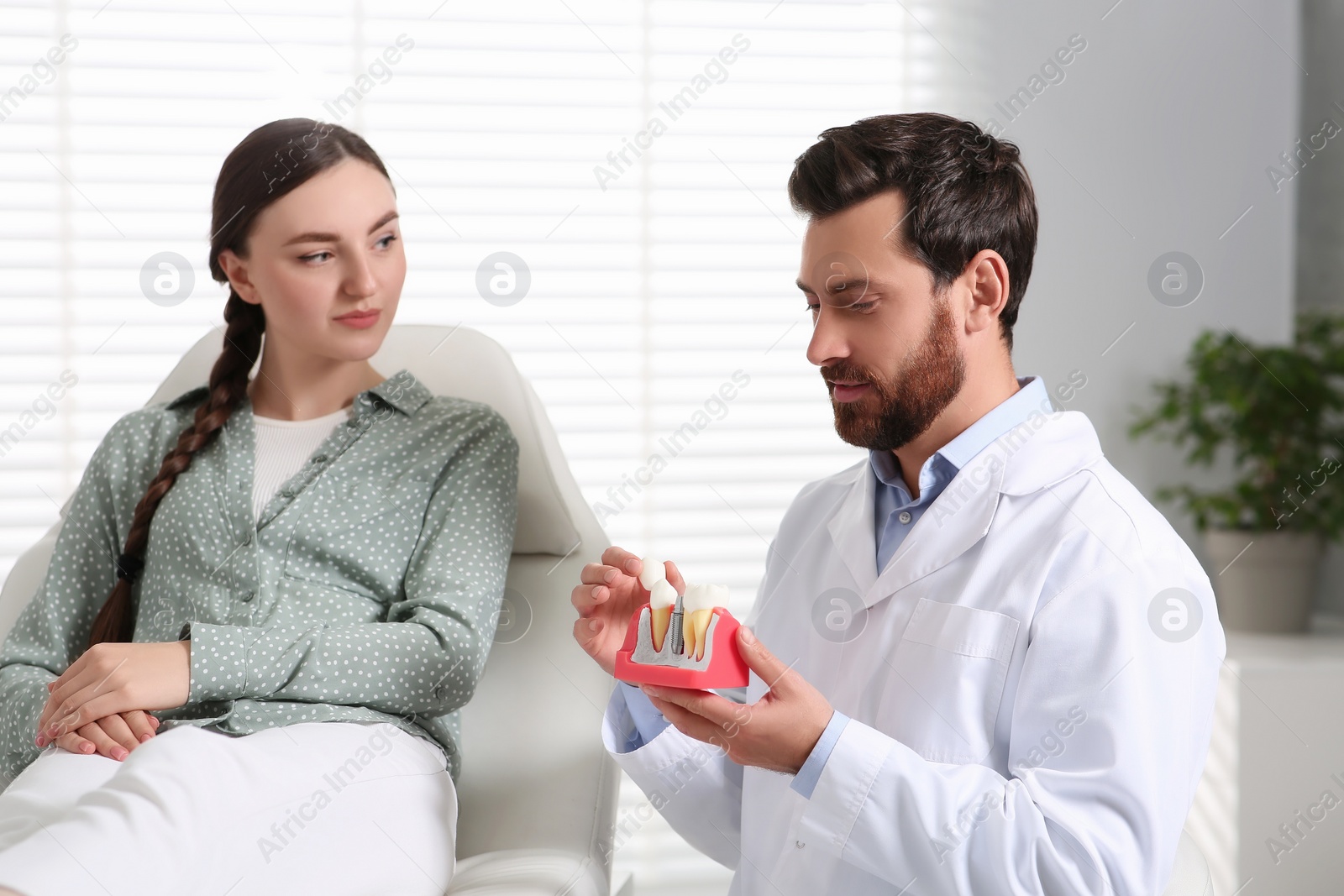 Photo of Doctor with educational model of dental implant consulting patient in clinic