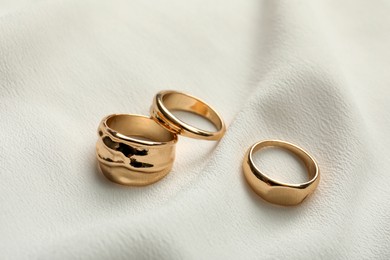 Photo of Elegant golden rings on white fabric. Stylish bijouterie