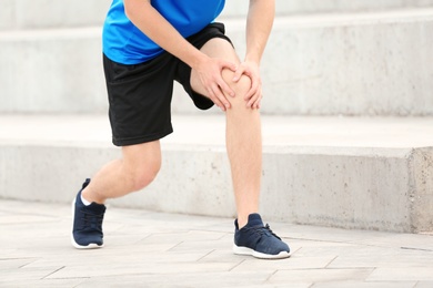 Photo of Man in sportswear suffering from knee pain on stairs, closeup