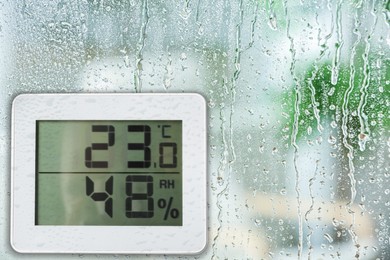 Digital hygrometer with thermometer on glass with water drops. Space for text