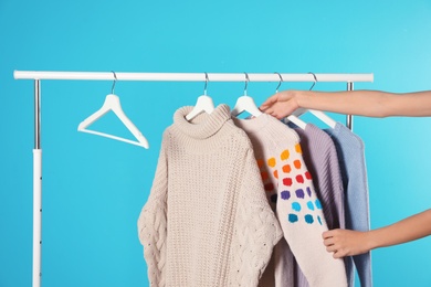 Woman choosing sweater on rack against color background