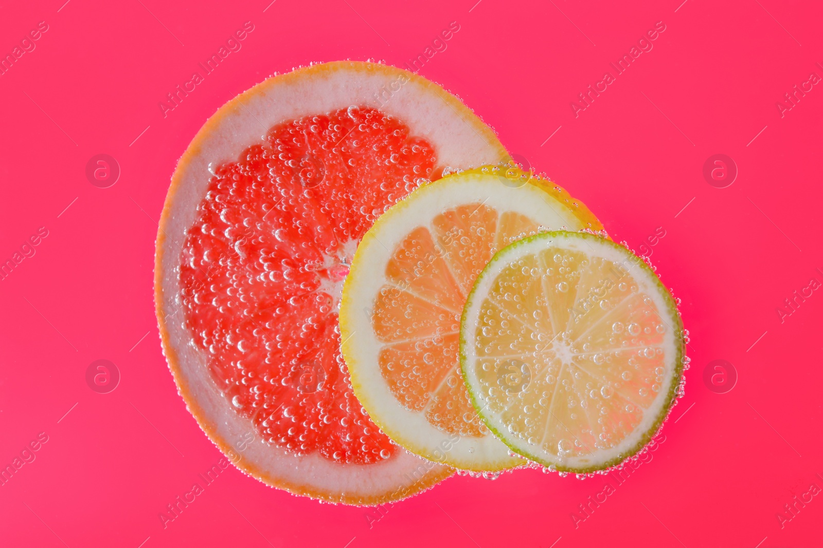 Photo of Slices of different citrus fruits in sparkling water on pink background