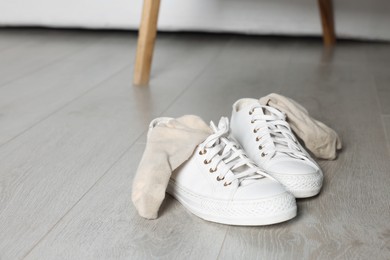 Photo of Sneakers with dirty socks on white wooden floor indoors