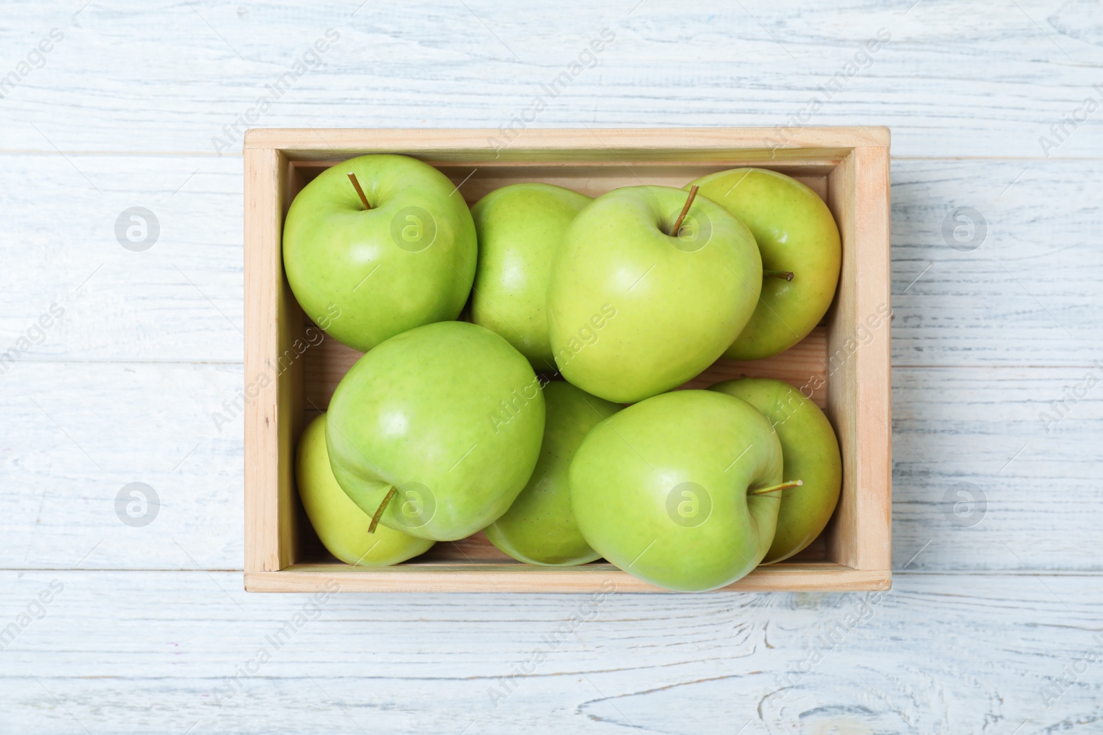 Photo of Wooden crate full of fresh green apples on light background, top view