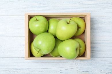 Wooden crate full of fresh green apples on light background, top view