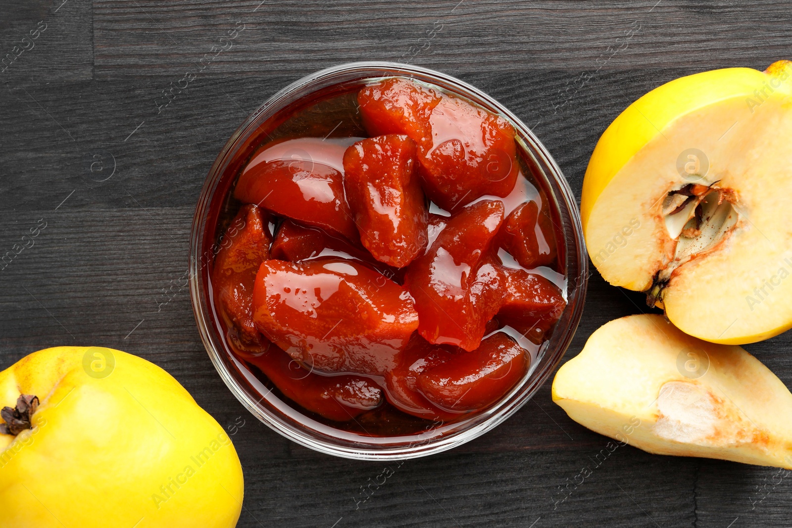 Photo of Quince jam in glass bowl and fresh raw fruits on grey wooden table, flat lay