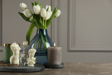 Beautiful sculptural candles, flowers and decor on grey table. Space for text
