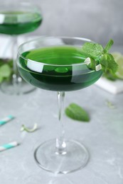 Delicious mint liqueur with green leaves on light grey marble table, closeup