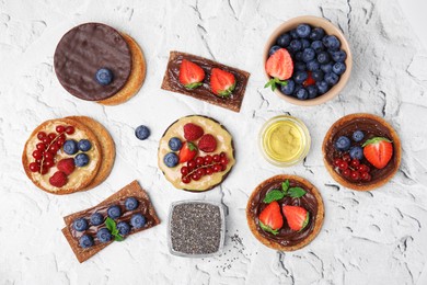 Fresh rye crispbreads, crunchy rice cakes and rusks with different toppings on white textured table, flat lay