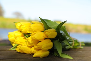 Bouquet of beautiful yellow tulips on wooden table outdoors, closeup