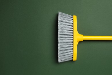 Plastic broom on dark green background, top view. Space for text