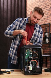 Photo of Man with screwdriver fixing coffee machine at table indoors