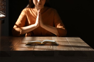 Religious woman praying over Bible at wooden table indoors, focus on book