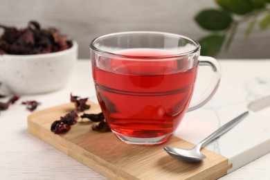 Photo of Cup of fresh hibiscus tea, dry flower leaves and spoon on wooden table