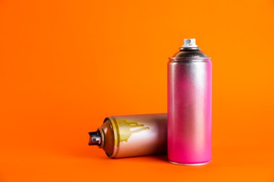 Used cans of spray paint on orange background. Space for text