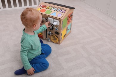 Photo of Cute little boy playing with busy board house on floor at home
