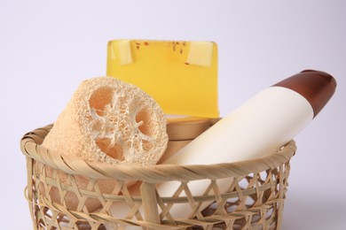 Wicker basket with loofah sponge and cosmetic products on white background, closeup