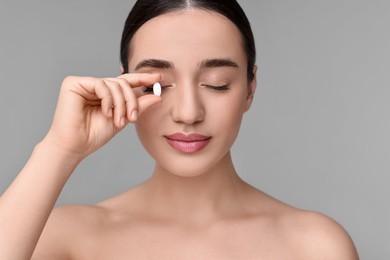 Photo of Beautiful young woman with vitamin pill on grey background