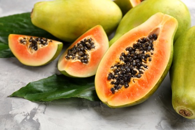 Fresh ripe papaya fruits with green leaves on grey table, closeup