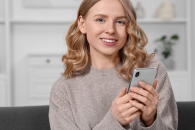Beautiful woman with blonde hair holding smartphone on sofa indoors