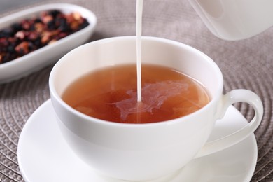 Photo of Pouring milk into cup with aromatic tea at table, closeup