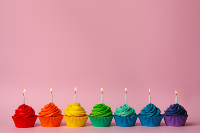 Delicious birthday cupcakes with burning candles on pink background