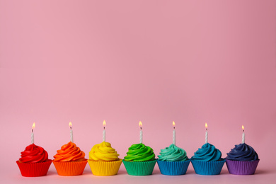 Photo of Delicious birthday cupcakes with burning candles on pink background