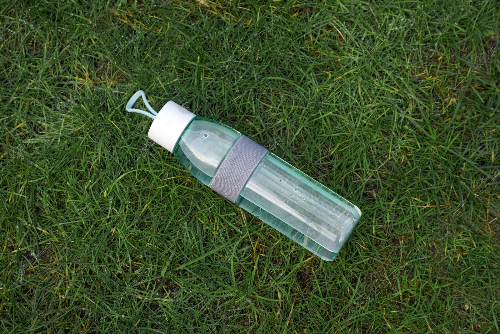 Photo of Bottle of water on green grass, top view. Morning exercise