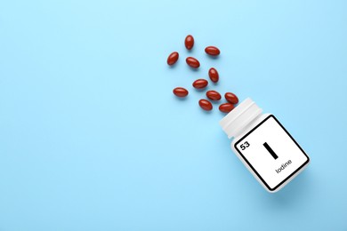 Photo of Plastic jar and iodine pills on light blue background, flat lay. Space for text