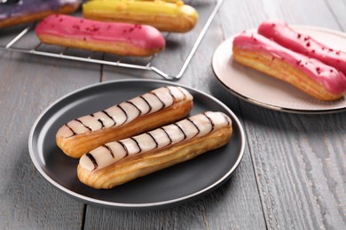 Photo of Different tasty glazed eclairs on wooden rustic table, closeup