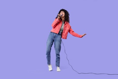 Photo of Beautiful young woman with microphone singing on purple background