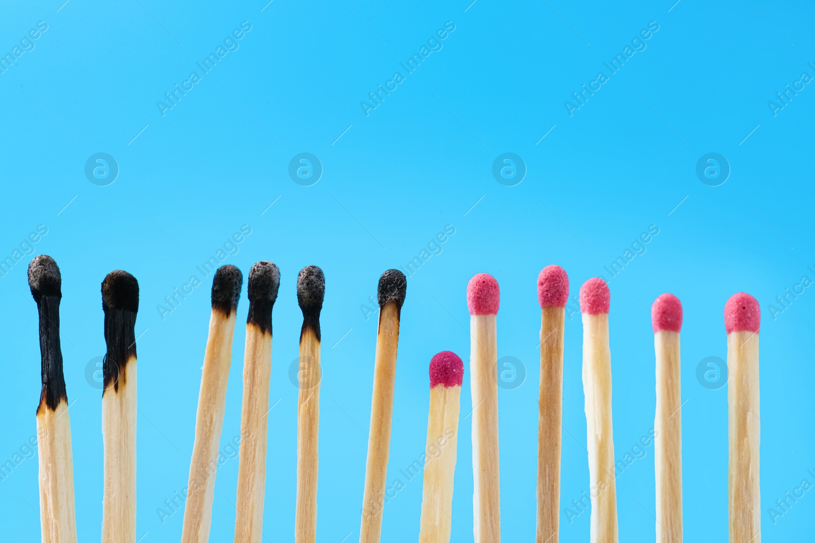 Photo of Burnt and whole matches on light blue background. Space for text