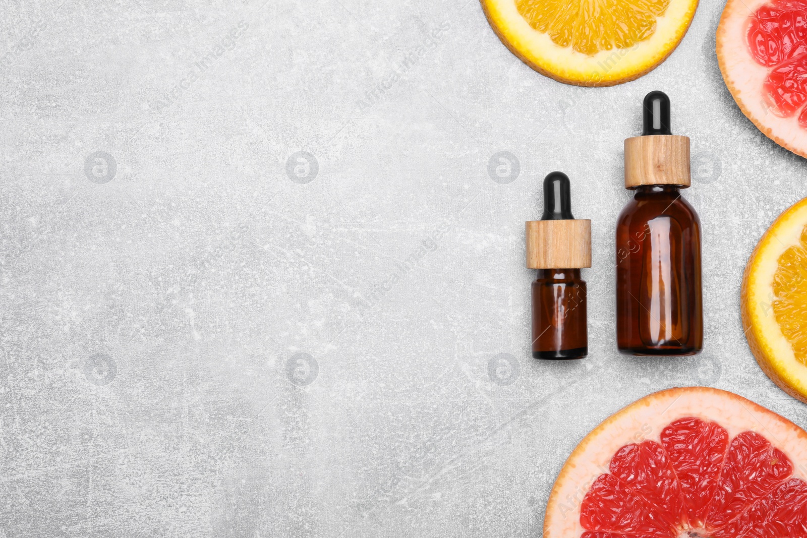 Photo of Bottles of essential oils with different citrus fruit slices on grey table, flat lay. Space for text