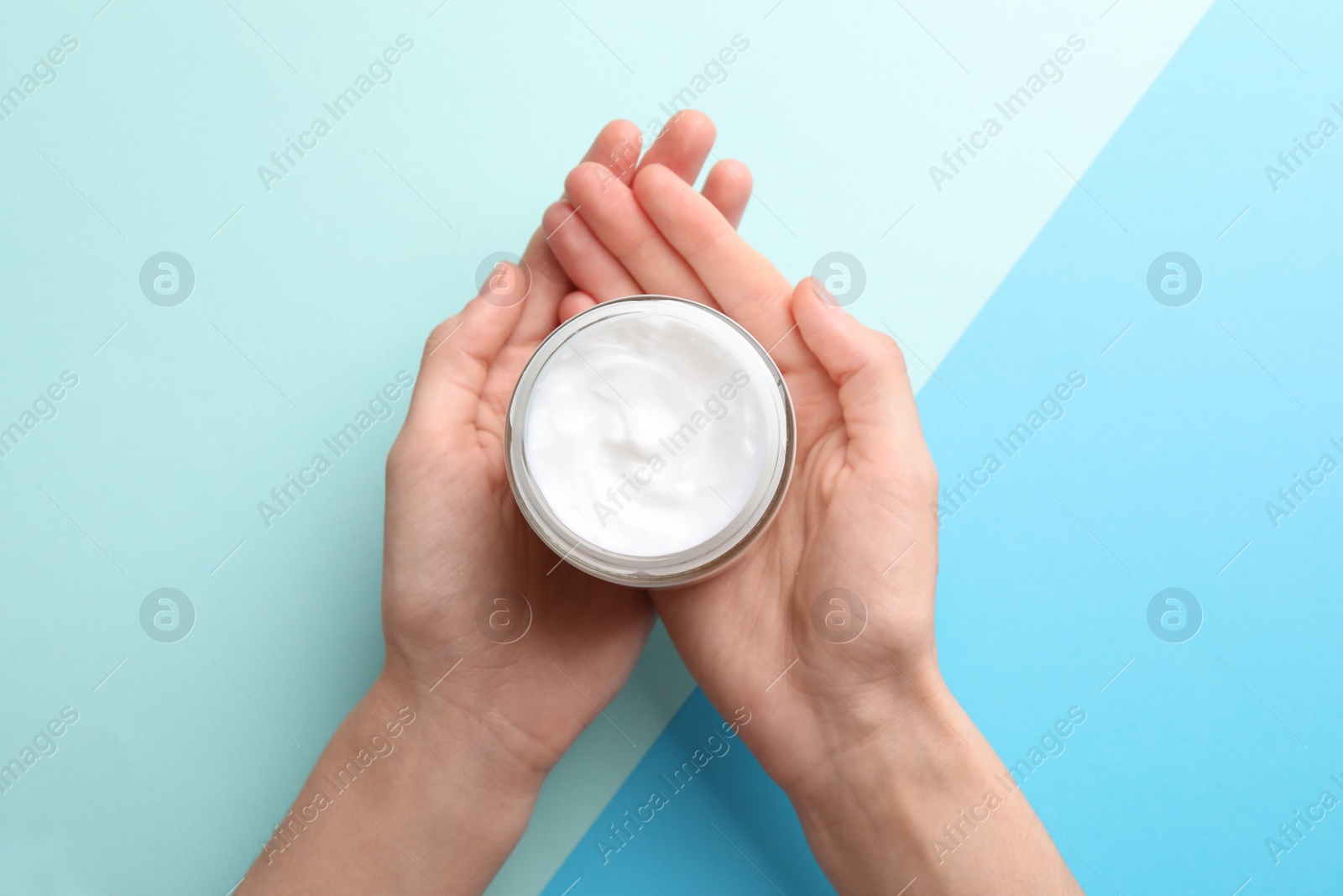 Photo of Woman holding jar of hand cream on color background, top view