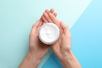 Photo of Woman holding jar of hand cream on color background, top view