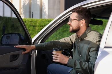 Photo of Coffee to go. Handsome man with paper cup of drink in car outdoors