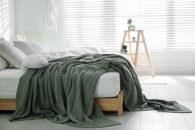 Comfortable bed with warm knitted plaid in stylish room interior