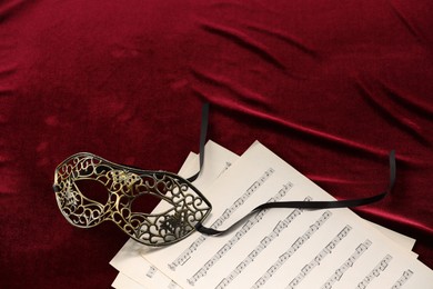 Photo of Elegant face mask and music sheets on red fabric, space for text. Theatrical performance