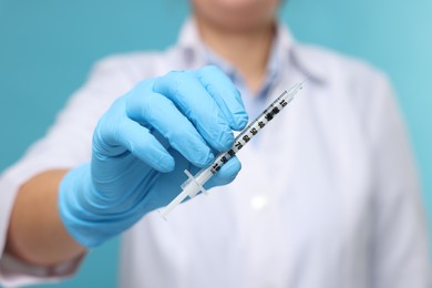 Photo of Doctor holding syringe on light blue background, closeup