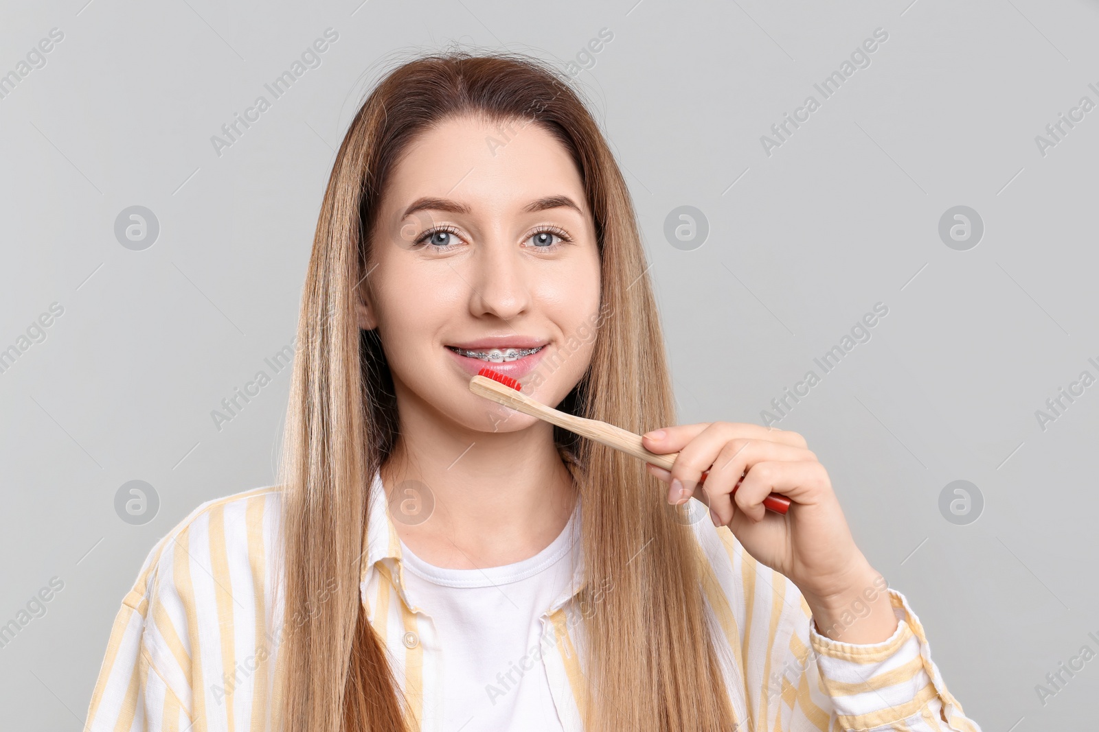 Photo of Smiling woman with dental braces cleaning teeth on grey background