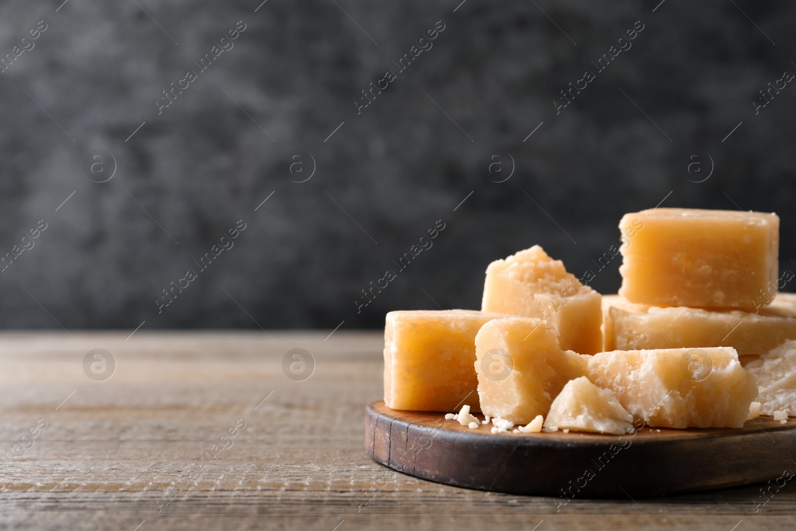 Photo of Pieces of delicious parmesan cheese on wooden table. Space for text