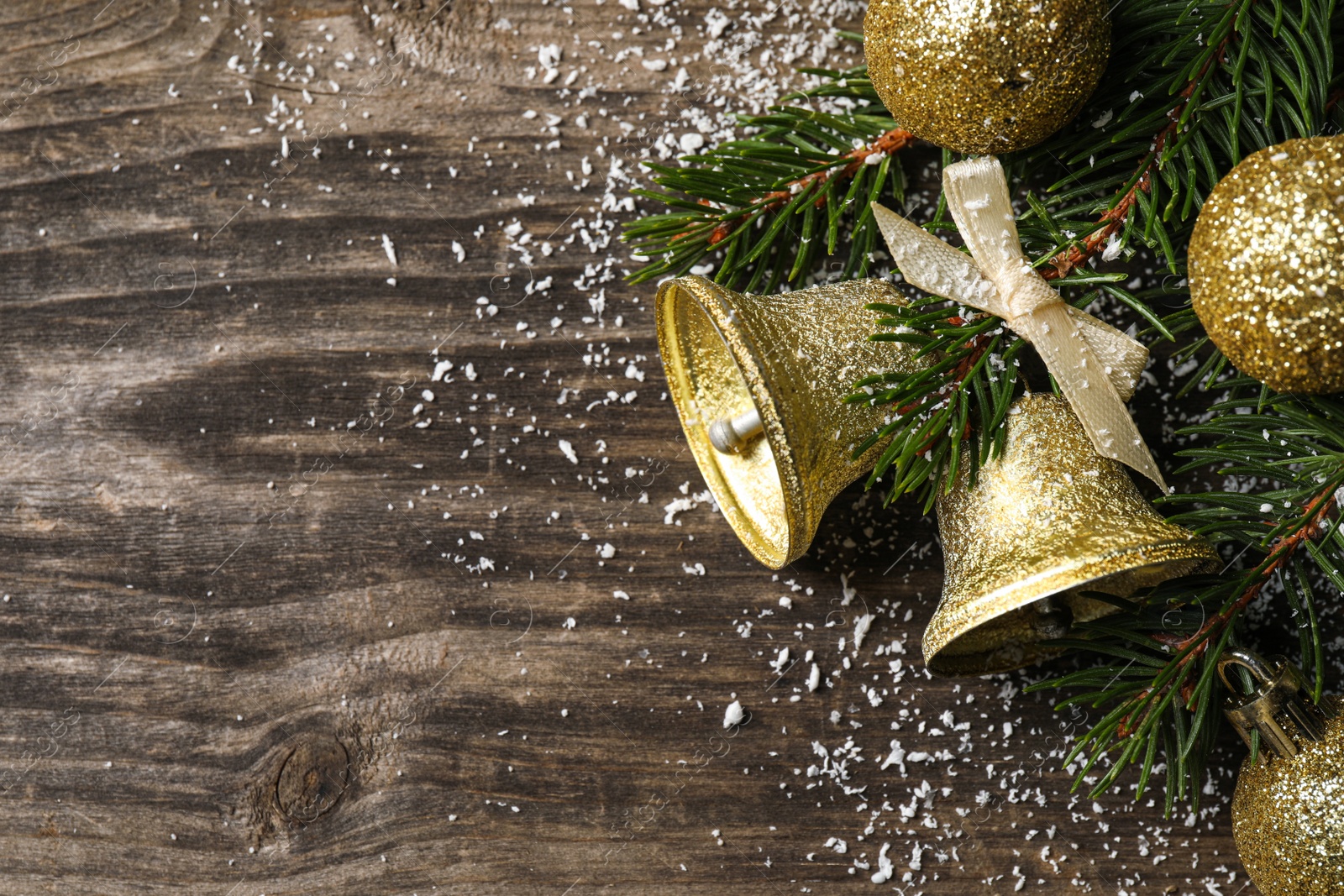 Photo of Christmas bells and fir tree branches with festive decor on wooden table, flat lay. Space for text