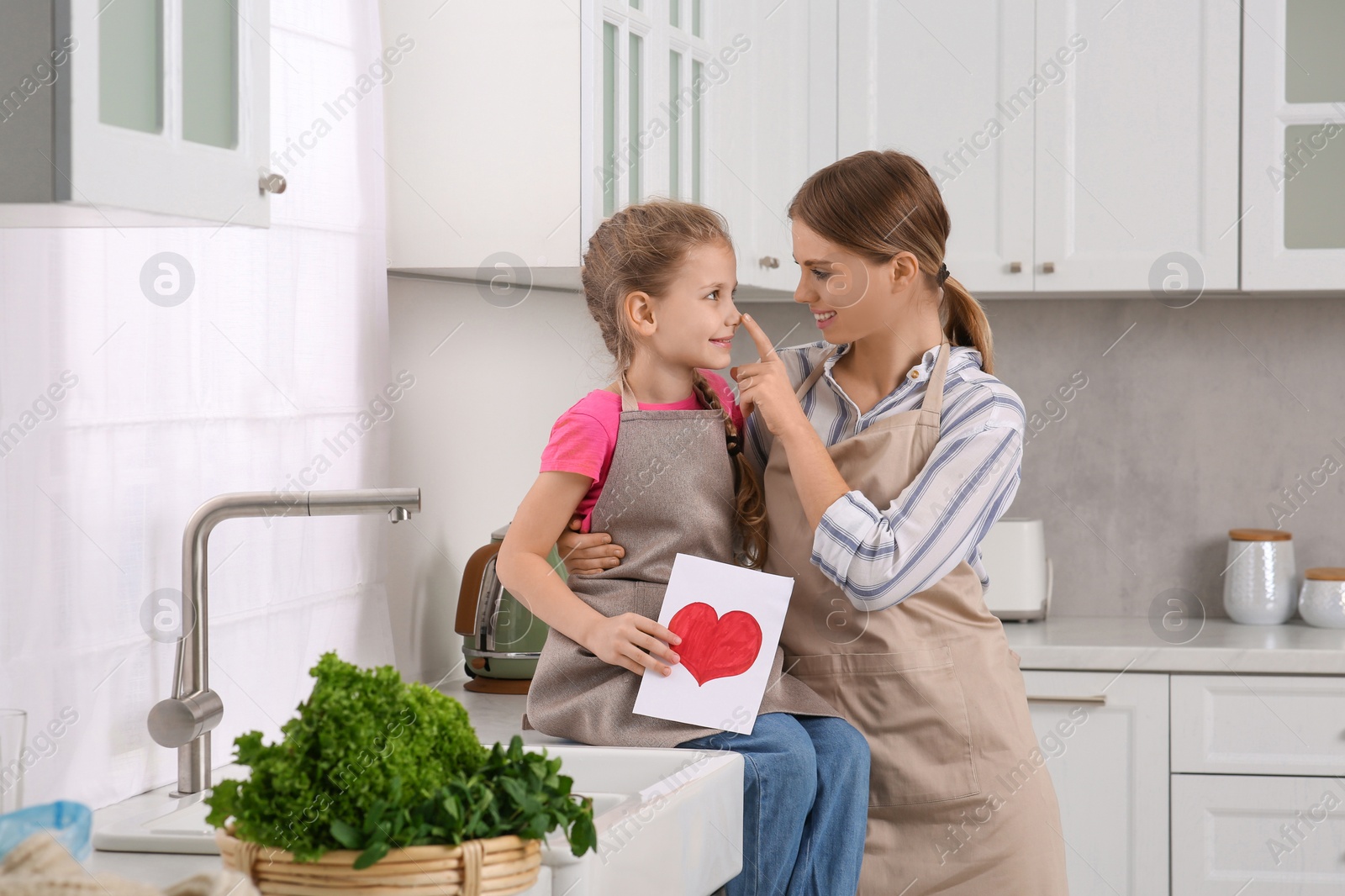 Photo of Little daughter congratulating mom with greeting card in kitchen. Happy Mother's Day