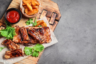 Photo of Delicious grilled ribs and garnish on grey table, top view. Space for text