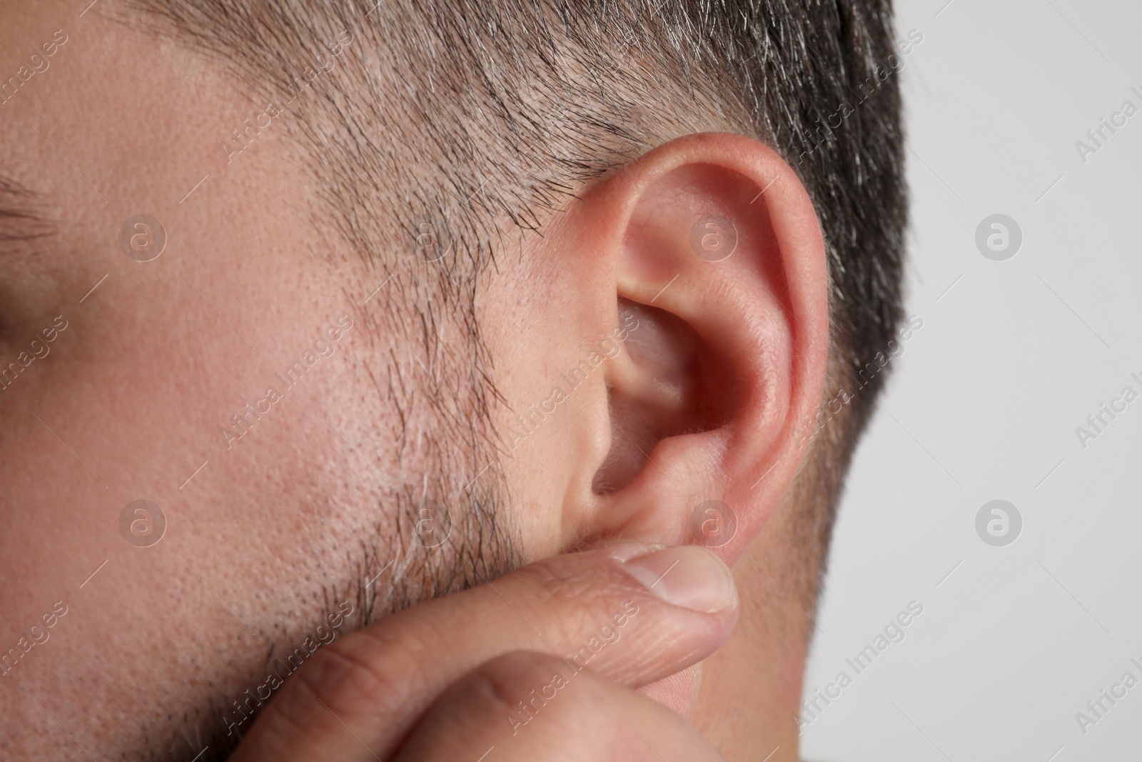 Photo of Man touching his ear on light grey background, closeup