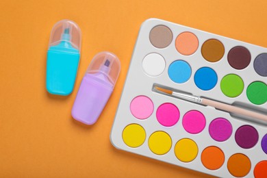 Photo of Watercolor palette with brush and markers on pale orange background, flat lay