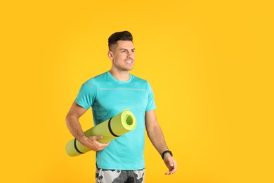 Photo of Handsome man with yoga mat on yellow background